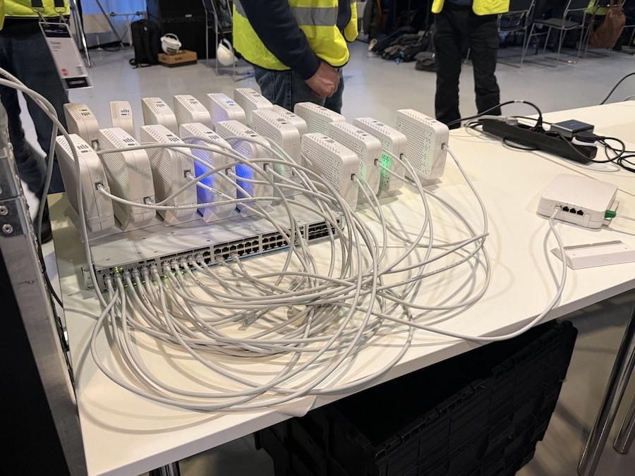 Wireless Active Testing setup process. Multiple Cisco CW9172H access points, connected to a Cisco Switch on a staging table, with event staff visible in the background.